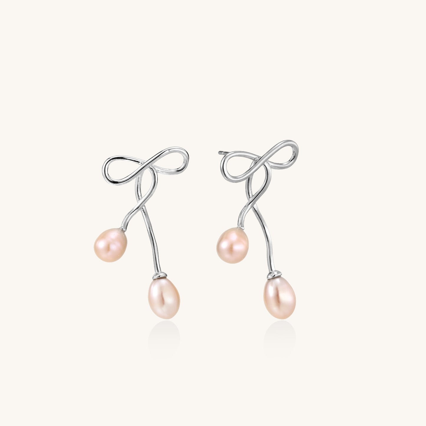 Delicate sterling silver wire earrings with organic bow shapes and two pink freshwater pearls on white background
