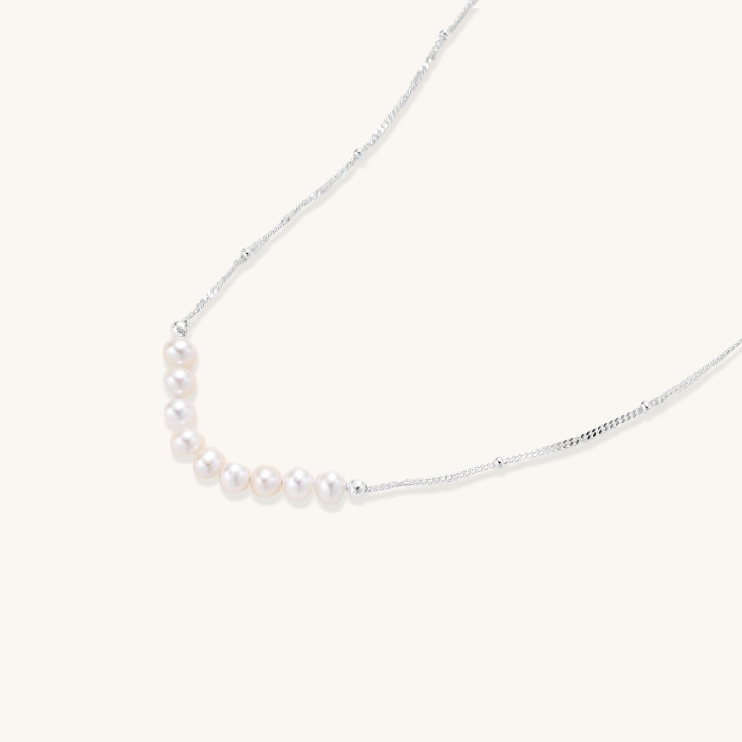 Delicate sterling silver chain with small white freshwater pearls arranged asymmetrically on white background.