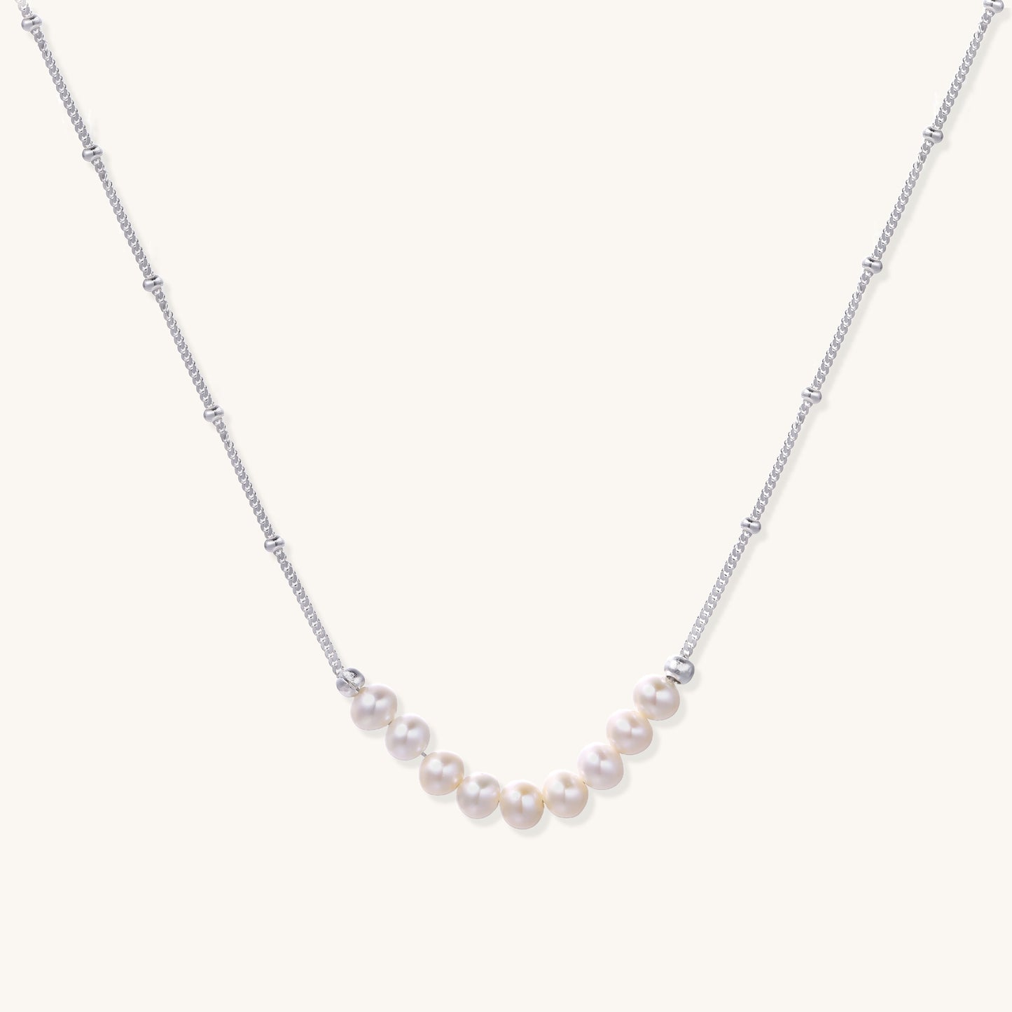 Delicate sterling silver chain with small white freshwater pearls arranged asymmetrically on white background.