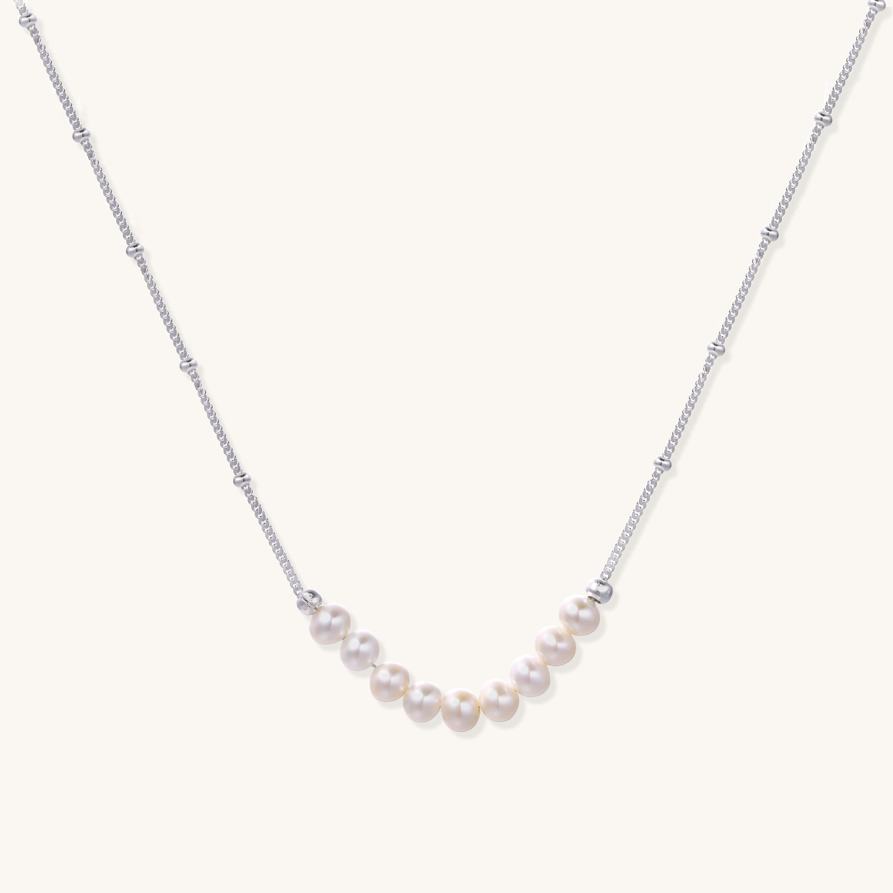 Delicate sterling silver chain with small white freshwater pearls arranged asymmetrically on white background.