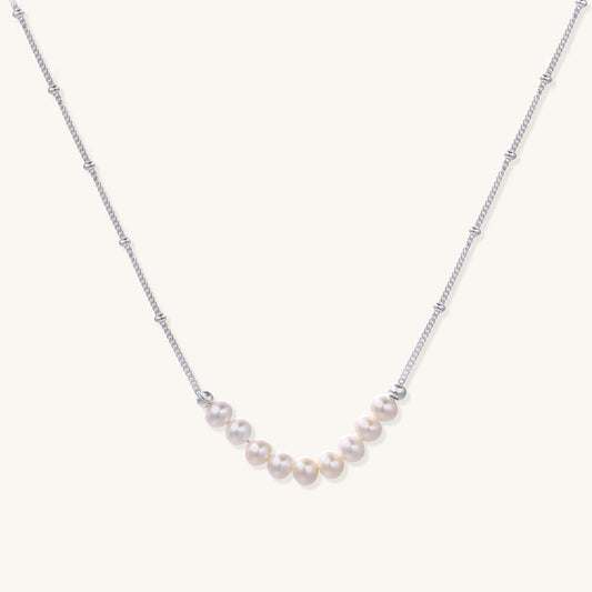 Delicate sterling silver chain with small white freshwater pearls arranged asymmetrically on white background.