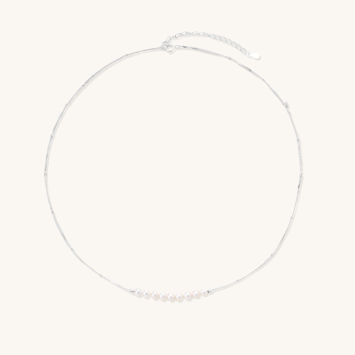 Delicate sterling silver chain with small white freshwater pearls arranged asymmetrically on white background.
