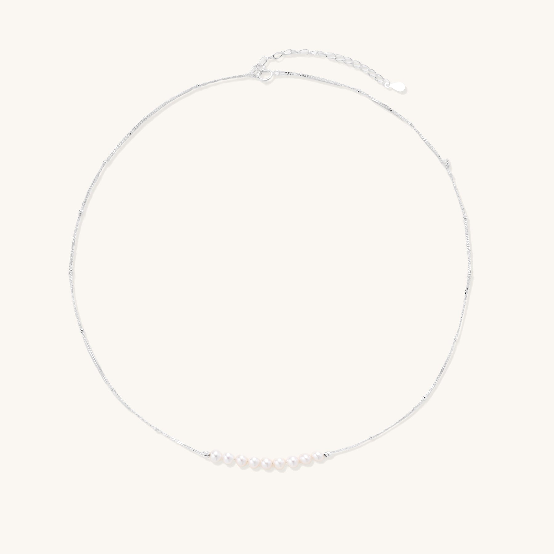 Delicate sterling silver chain with small white freshwater pearls arranged asymmetrically on white background.