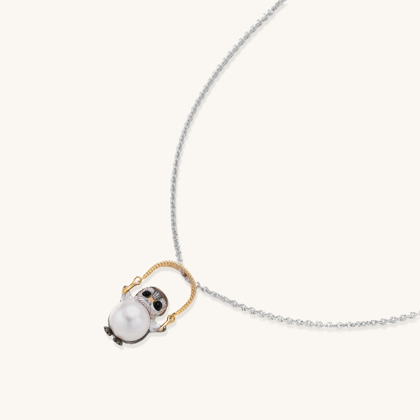 Silver owl pendant holding a round freshwater pearl on an adjustable chain against white background
