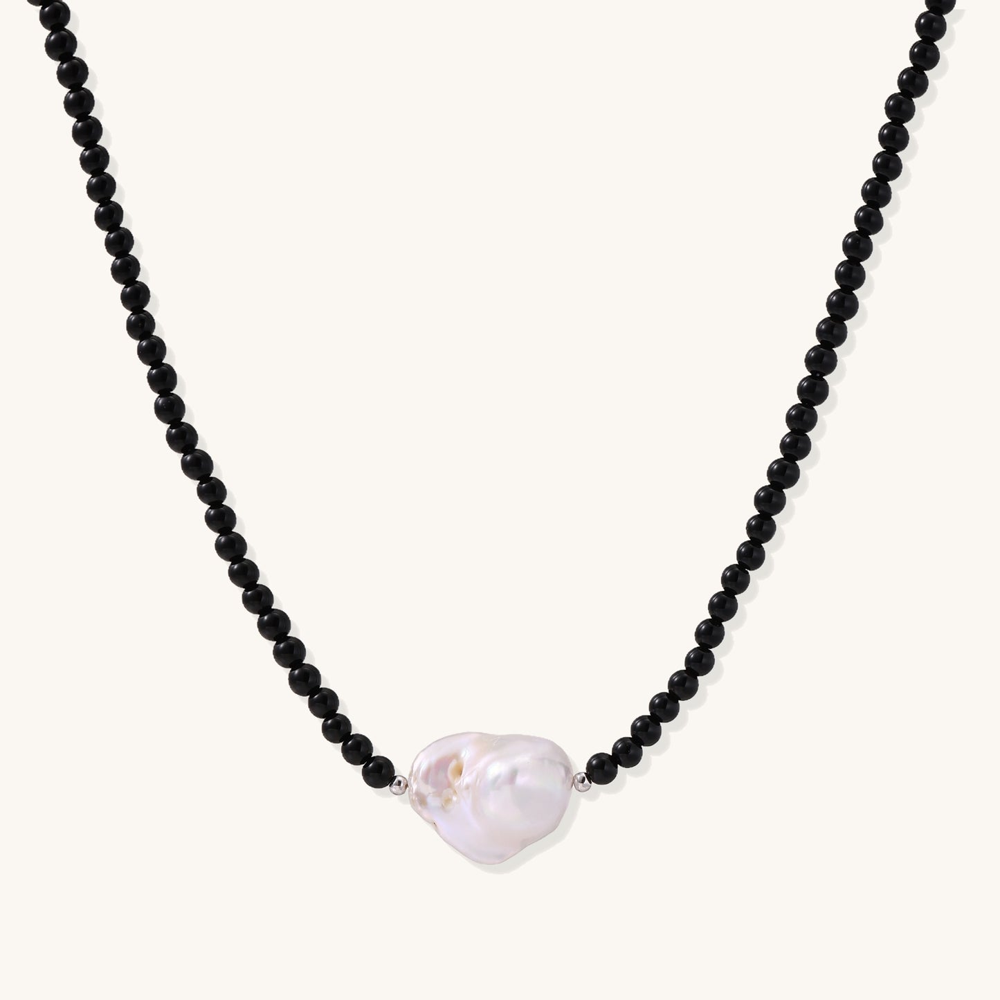 Elegant necklace with black agate beads and iridescent baroque freshwater pearl centerpiece on white background.