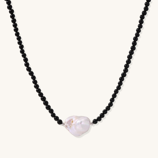 Elegant necklace with black agate beads and iridescent baroque freshwater pearl centerpiece on white background.