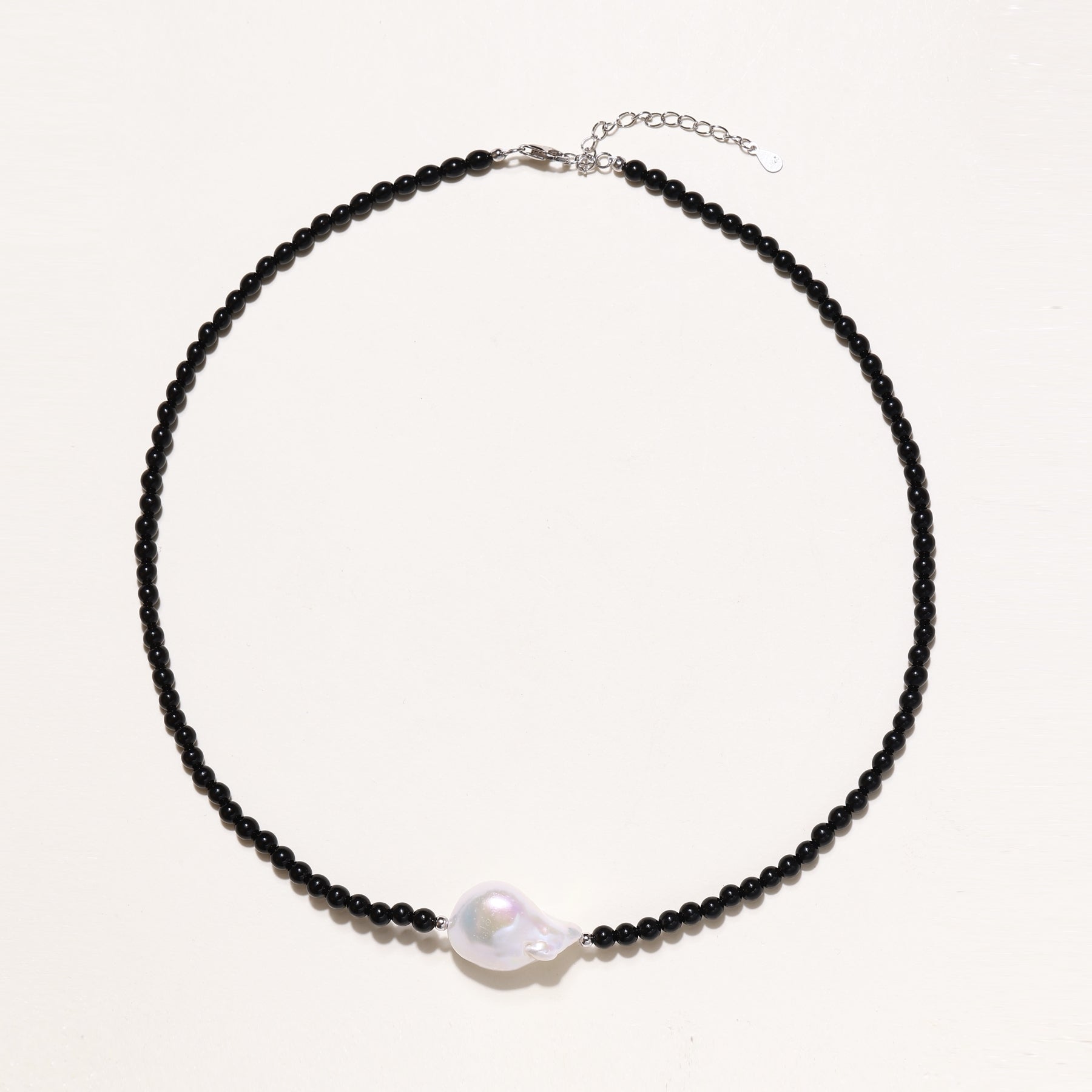 Elegant necklace with black agate beads and iridescent baroque freshwater pearl centerpiece on white background.