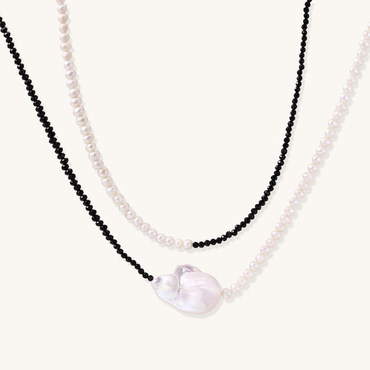 Two-strand necklace with black crystal beads and white pearls featuring a large baroque pearl centerpiece on white background.