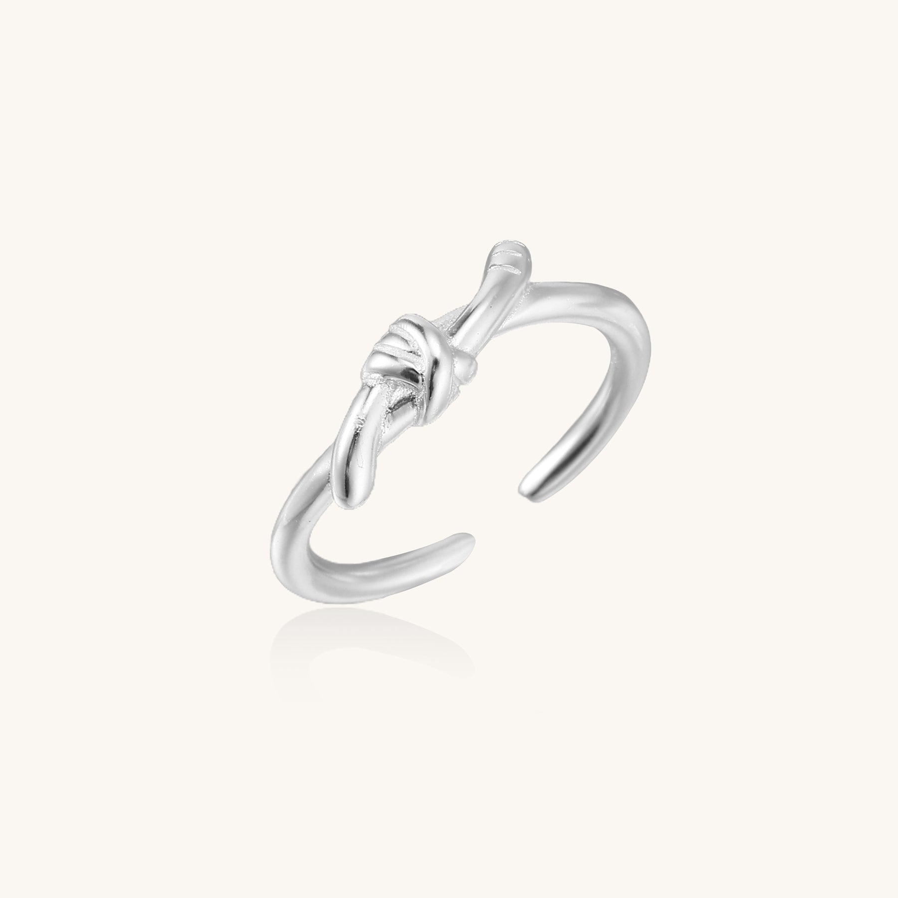 Delicate sterling silver ring with geometric knot design on white background, showcasing adjustable open band.