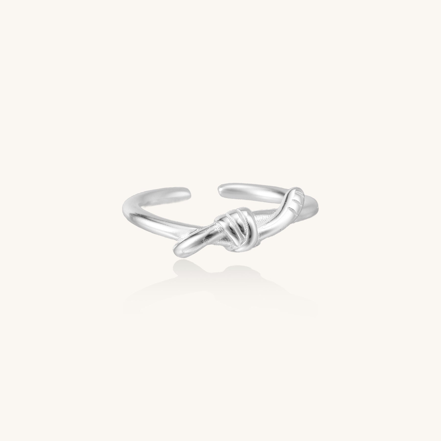 Delicate sterling silver ring with geometric knot design on white background, showcasing adjustable open band.