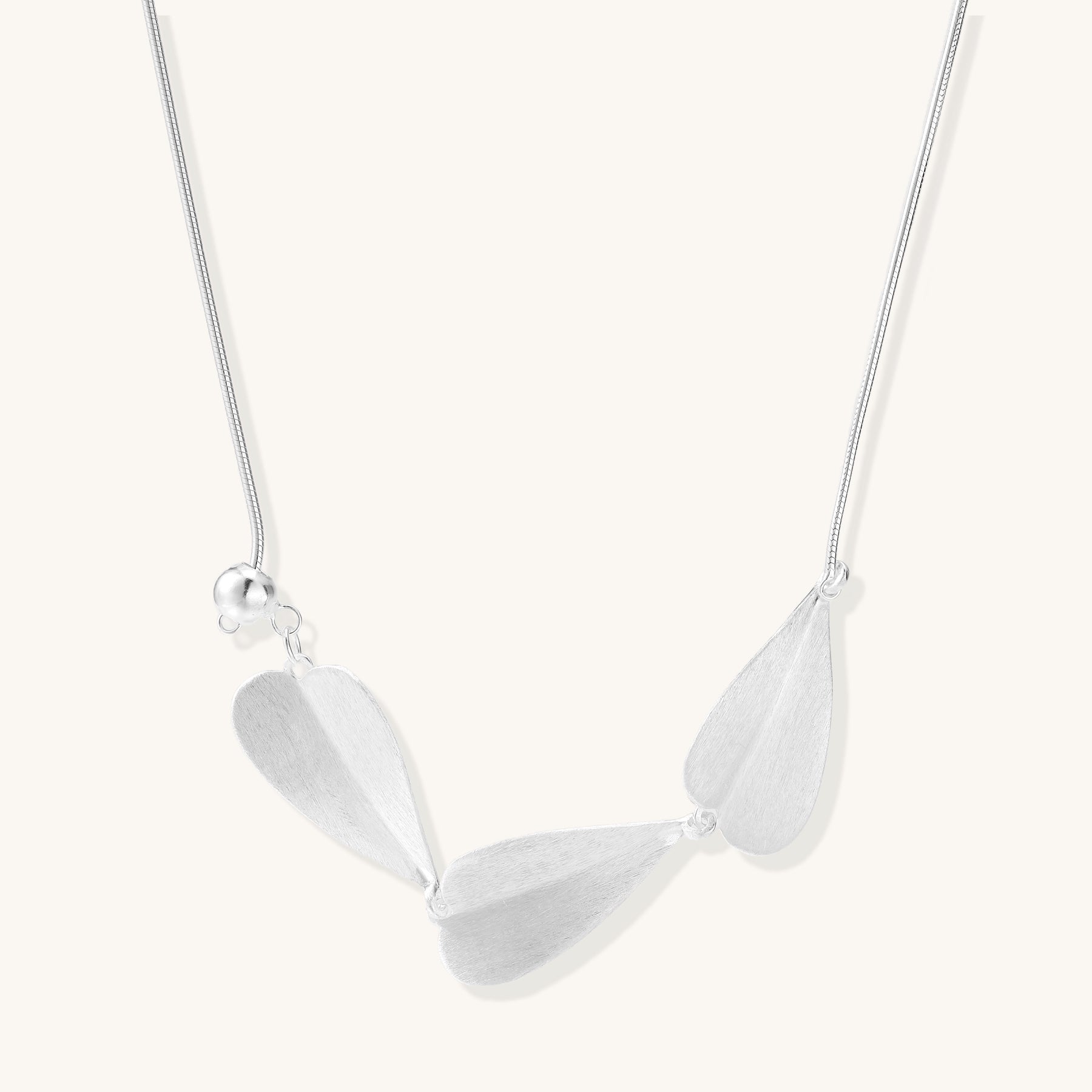 Delicate sterling silver necklace with brushed leaf pendants distributed along a fine chain on white background.