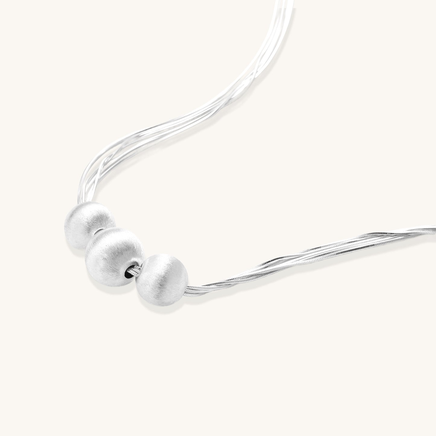 Multi-strand sterling silver necklace with three polished round beads clustered at center on white background.