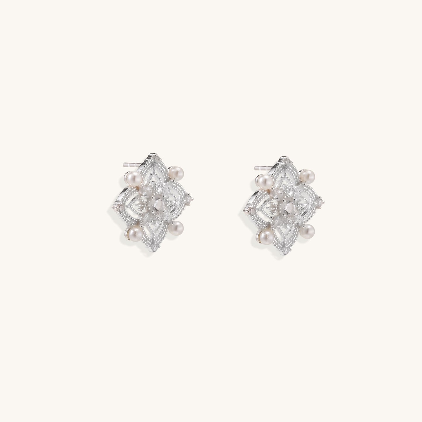 Detailed view of sterling silver stud earrings with geometric filigree design and small freshwater pearls on white background.