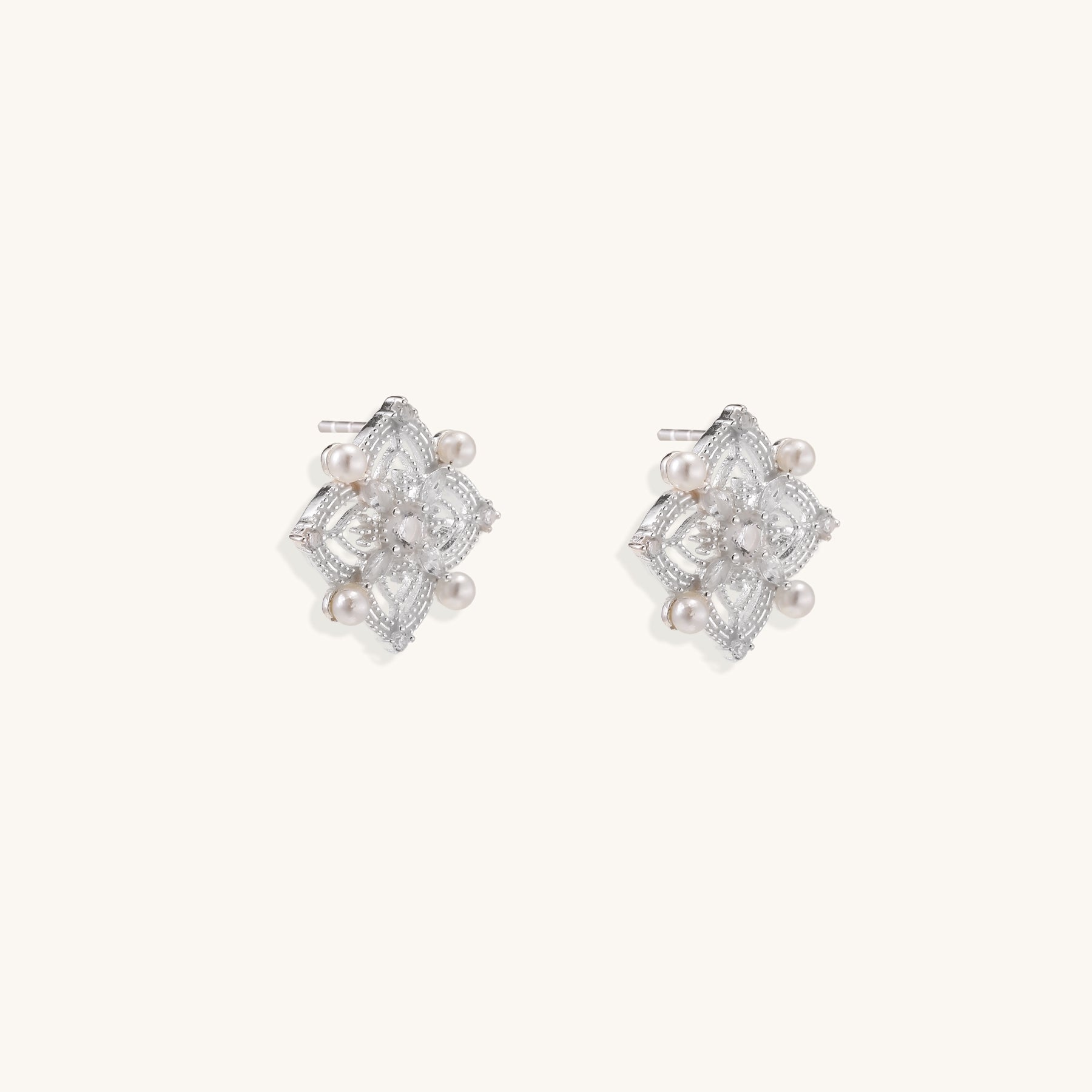 Detailed view of sterling silver stud earrings with geometric filigree design and small freshwater pearls on white background.