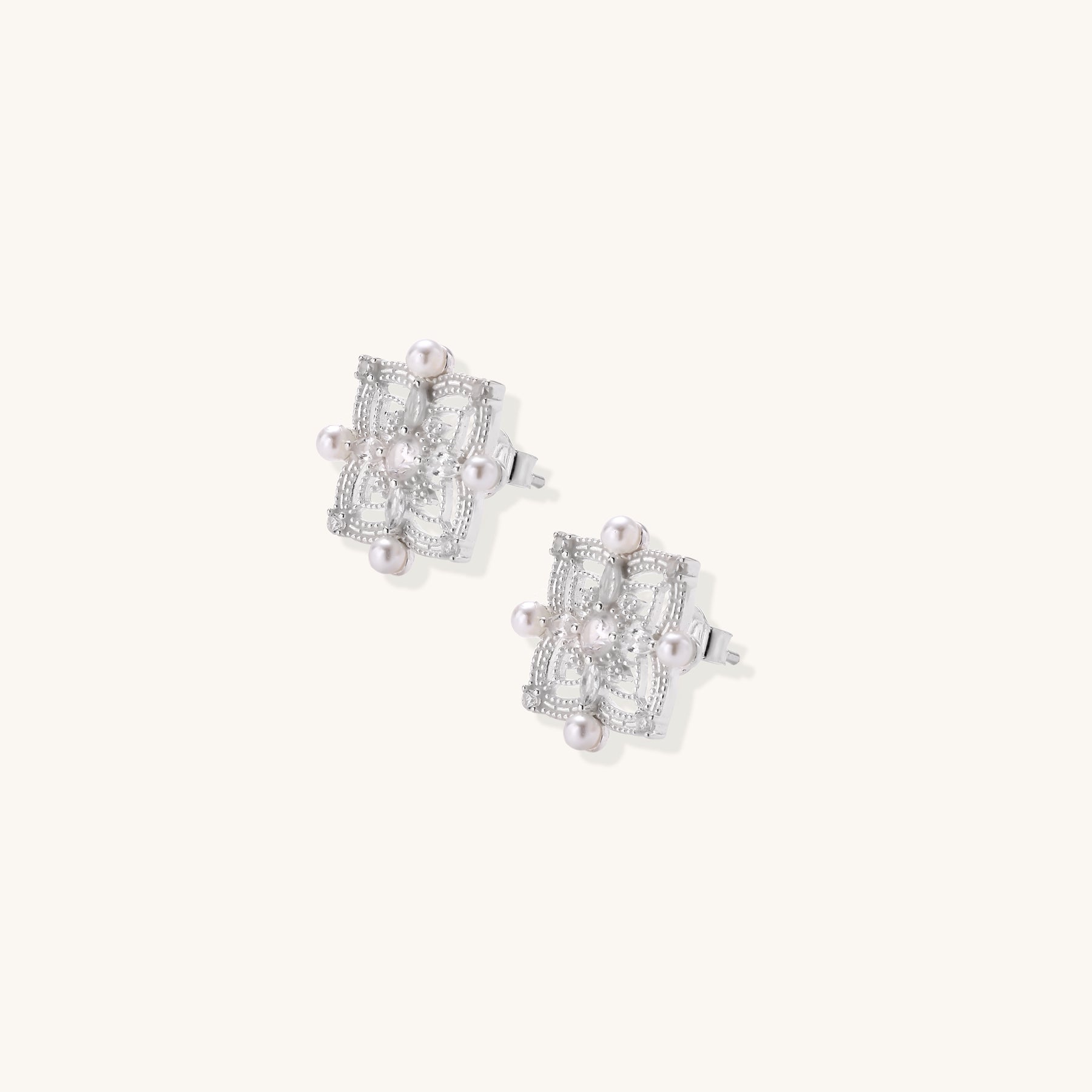 Detailed view of sterling silver stud earrings with geometric filigree design and small freshwater pearls on white background.