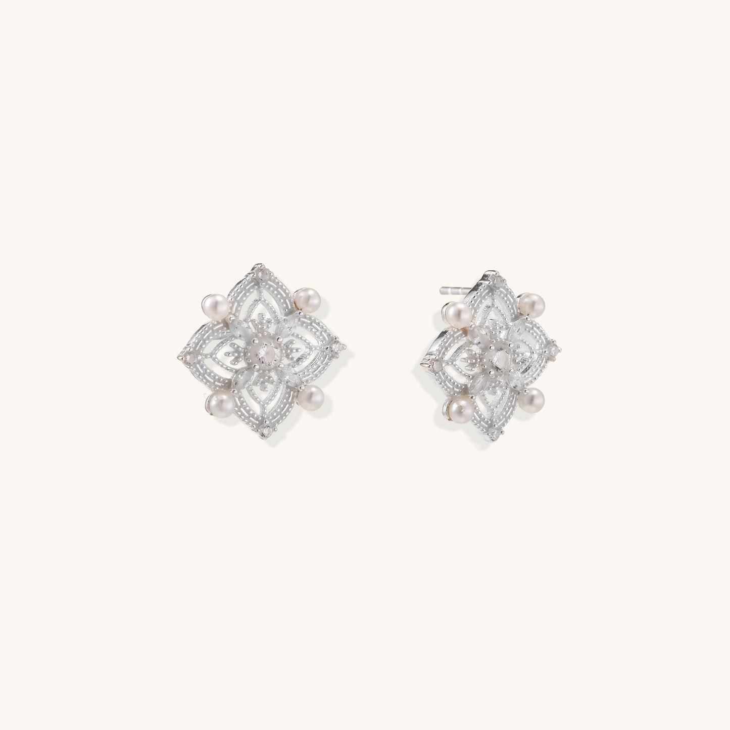 Detailed view of sterling silver stud earrings with geometric filigree design and small freshwater pearls on white background.