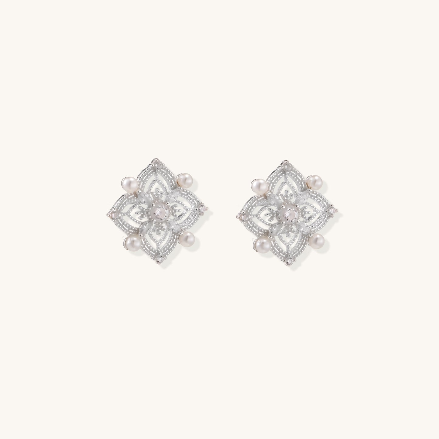 Detailed view of sterling silver stud earrings with geometric filigree design and small freshwater pearls on white background.
