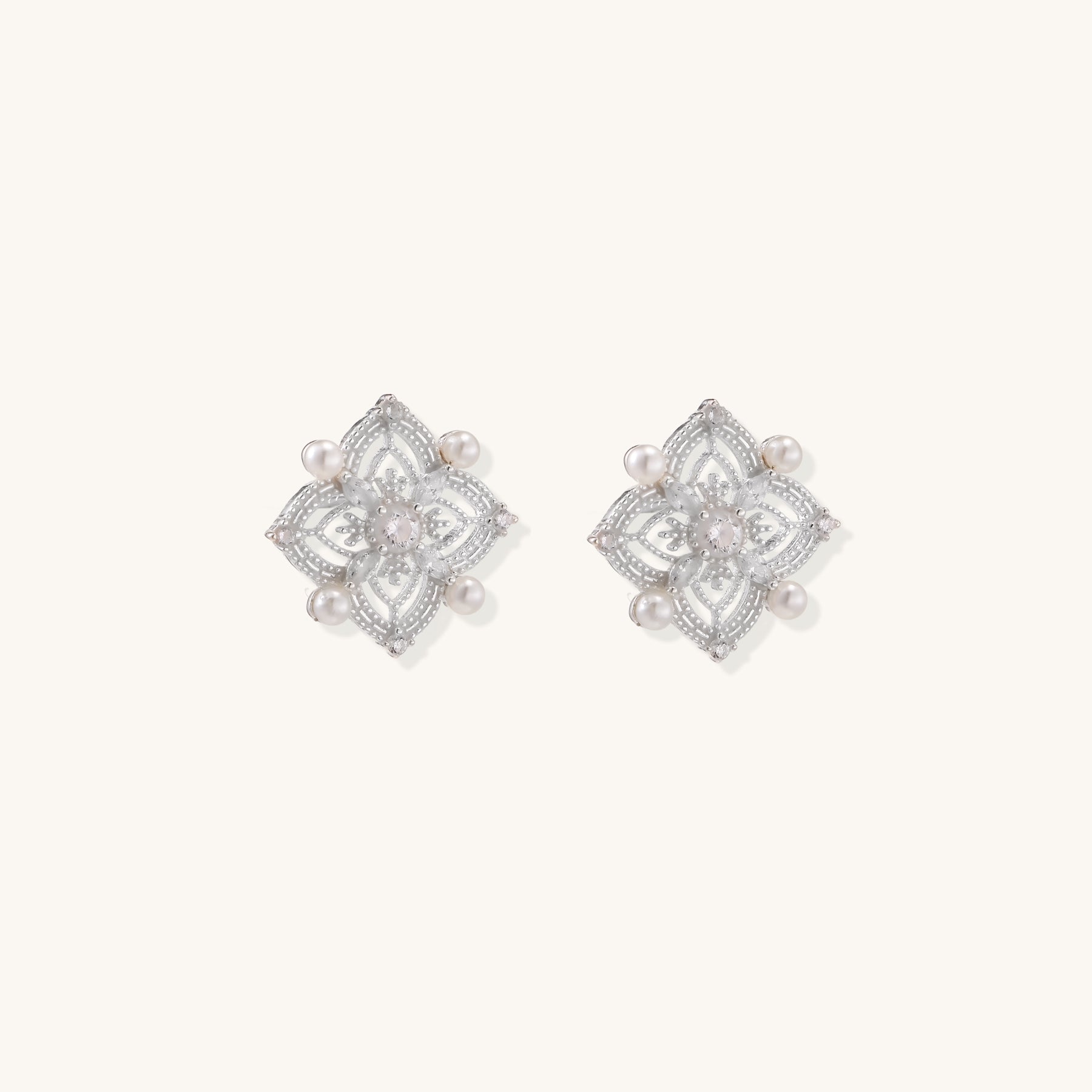 Detailed view of sterling silver stud earrings with geometric filigree design and small freshwater pearls on white background.