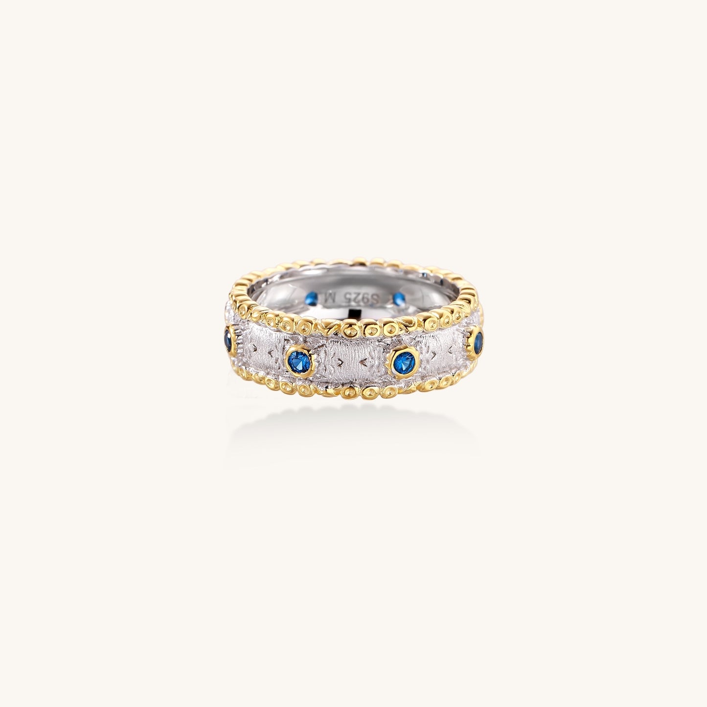 Sterling silver ring with brushed center band, blue zirconia stones, and 24k gold-plated decorative borders.