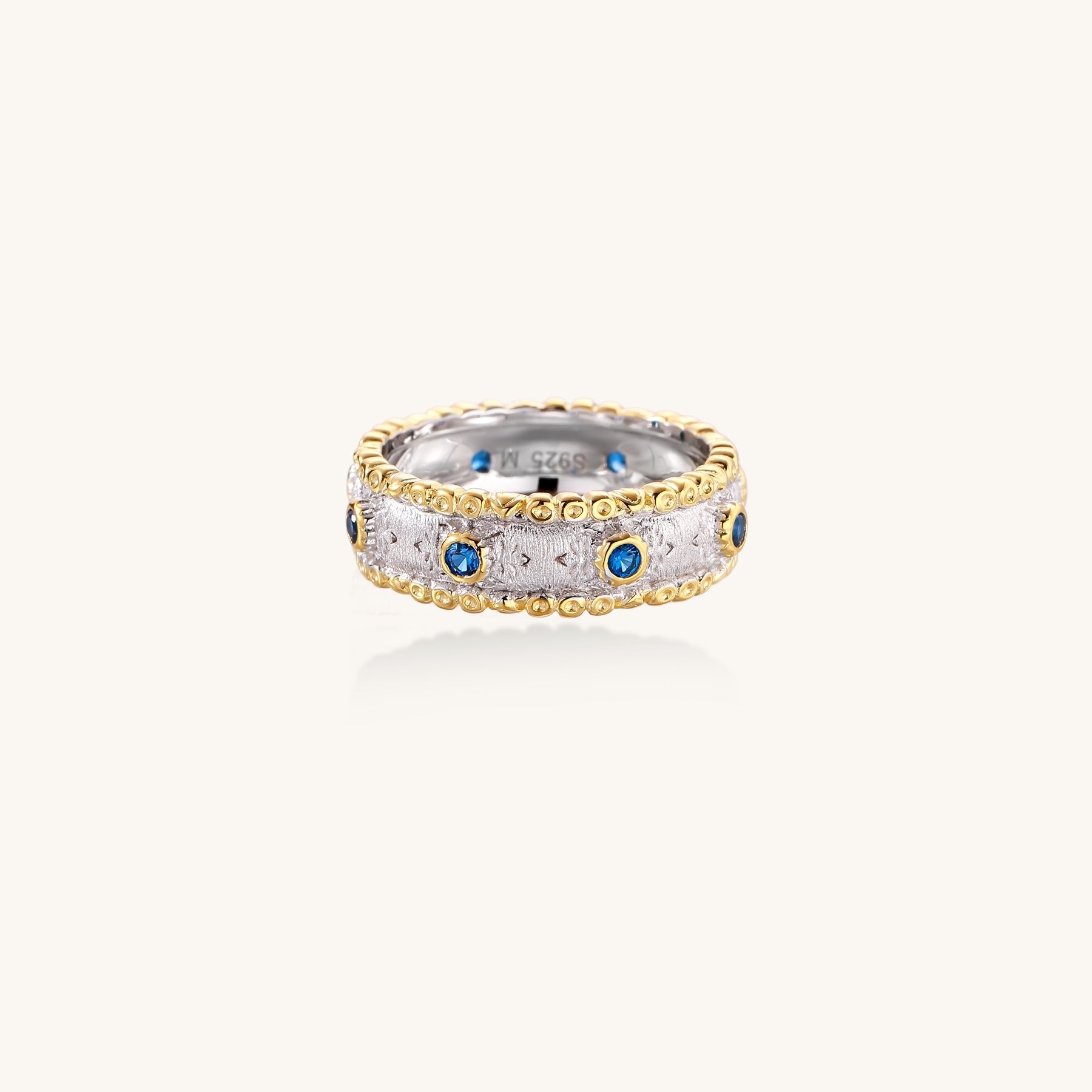 Sterling silver ring with brushed center band, blue zirconia stones, and 24k gold-plated decorative borders.