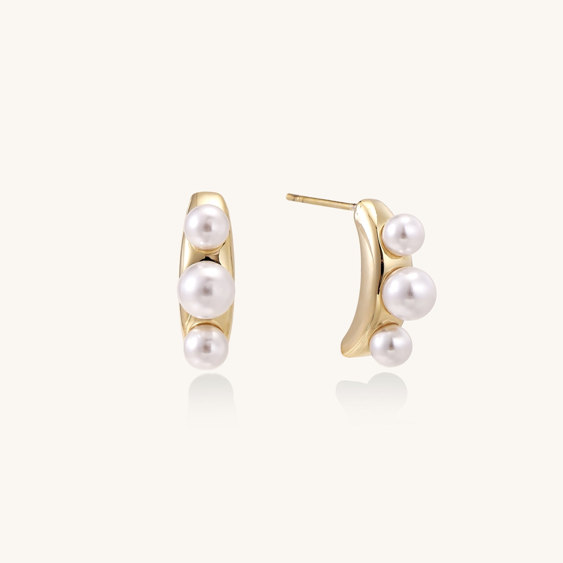 Delicate gold stud earrings with three lustrous white freshwater pearls arranged in an organic curved line.
