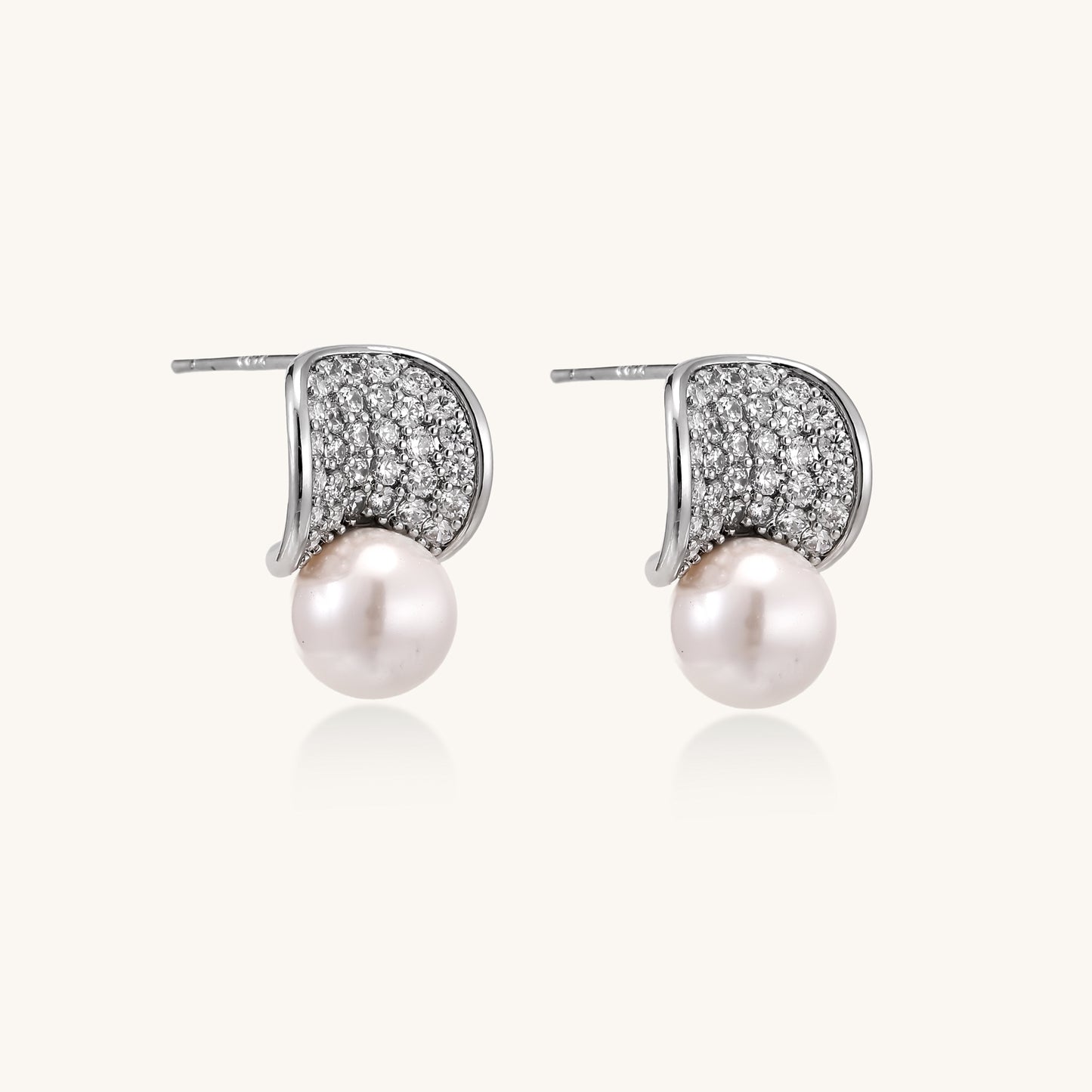 Elegant gold-plated curved earrings with diamond pavé crescents and suspended freshwater pearls on neutral background.