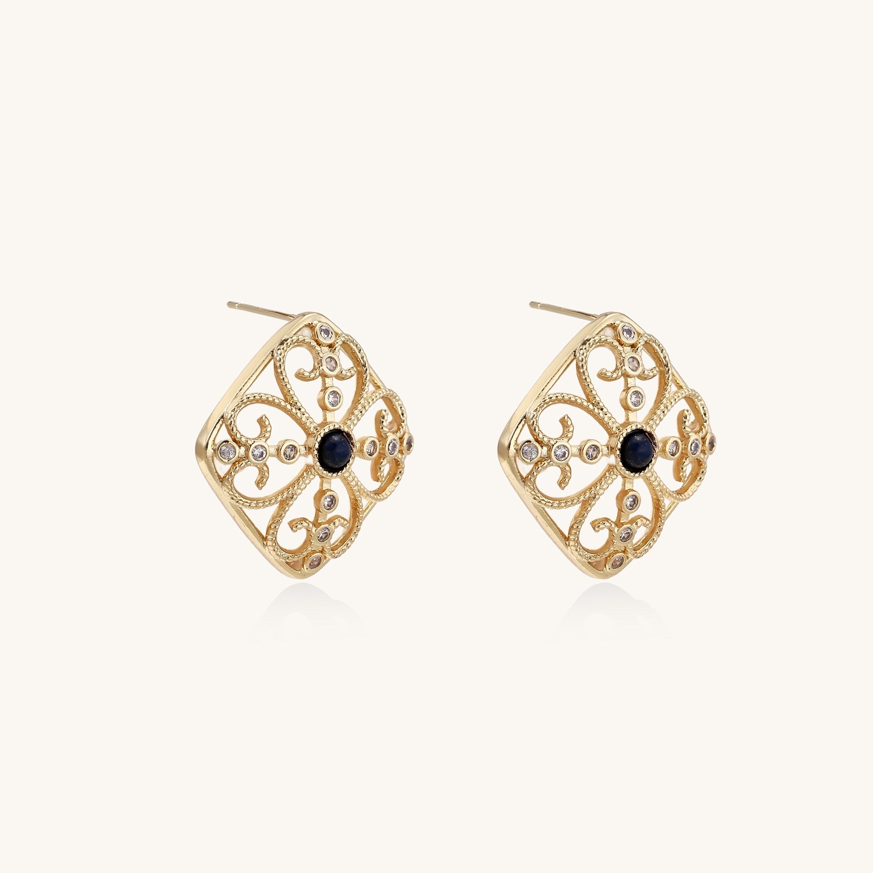 Ornate 18K gold plated stud earrings with intricate filigree design and central lapis lazuli stones on cream background.