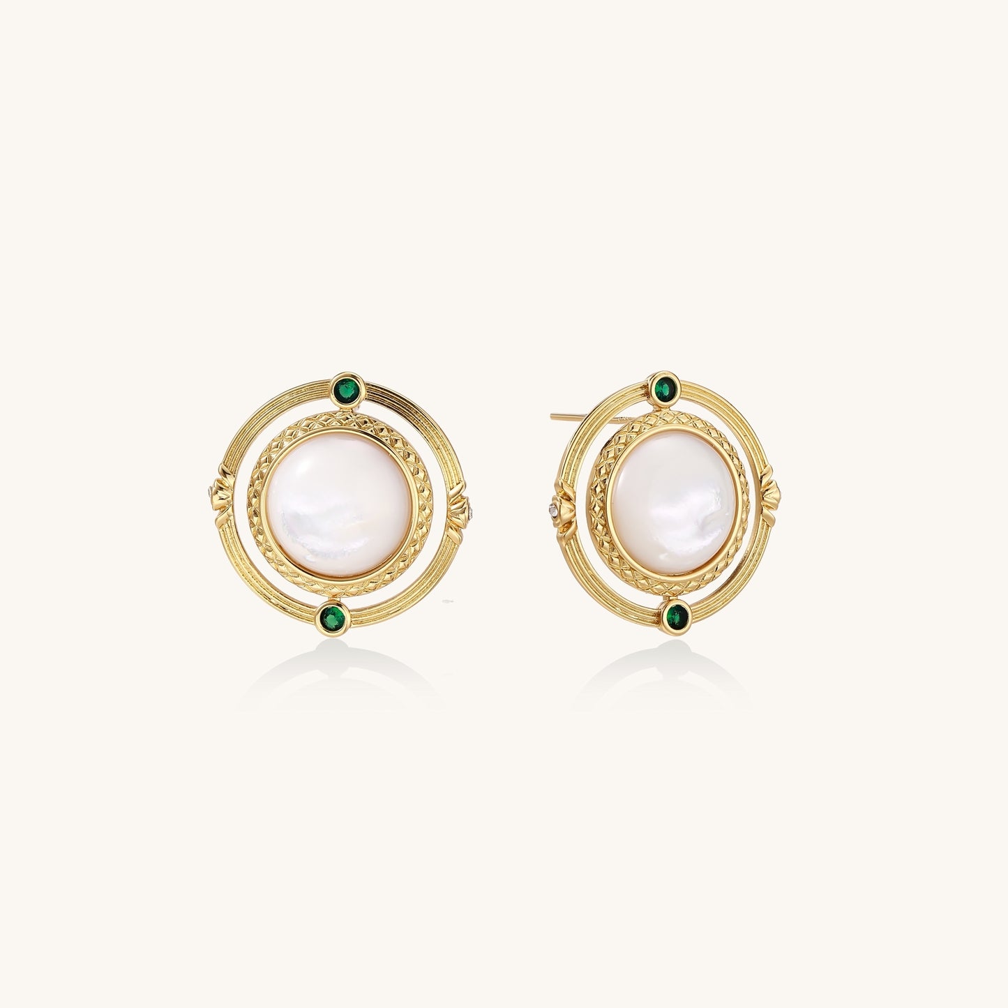 Close-up of gold-plated circular earrings with white mother-of-pearl centers and green zirconia accents on cream background.