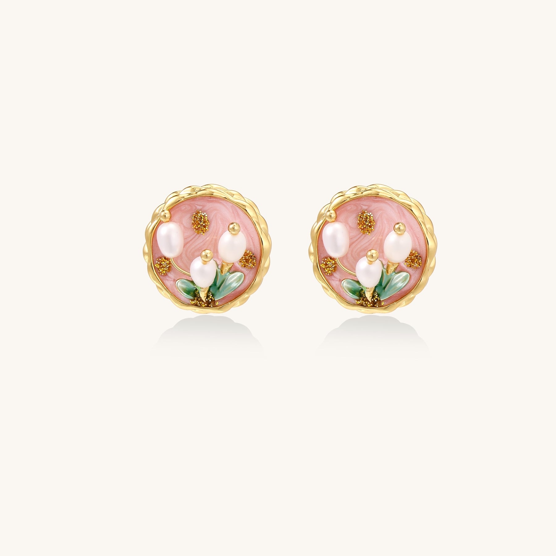 Round stud earrings with pink enamel background, white pearl tulips, green leaves, and twisted gold border on white background.