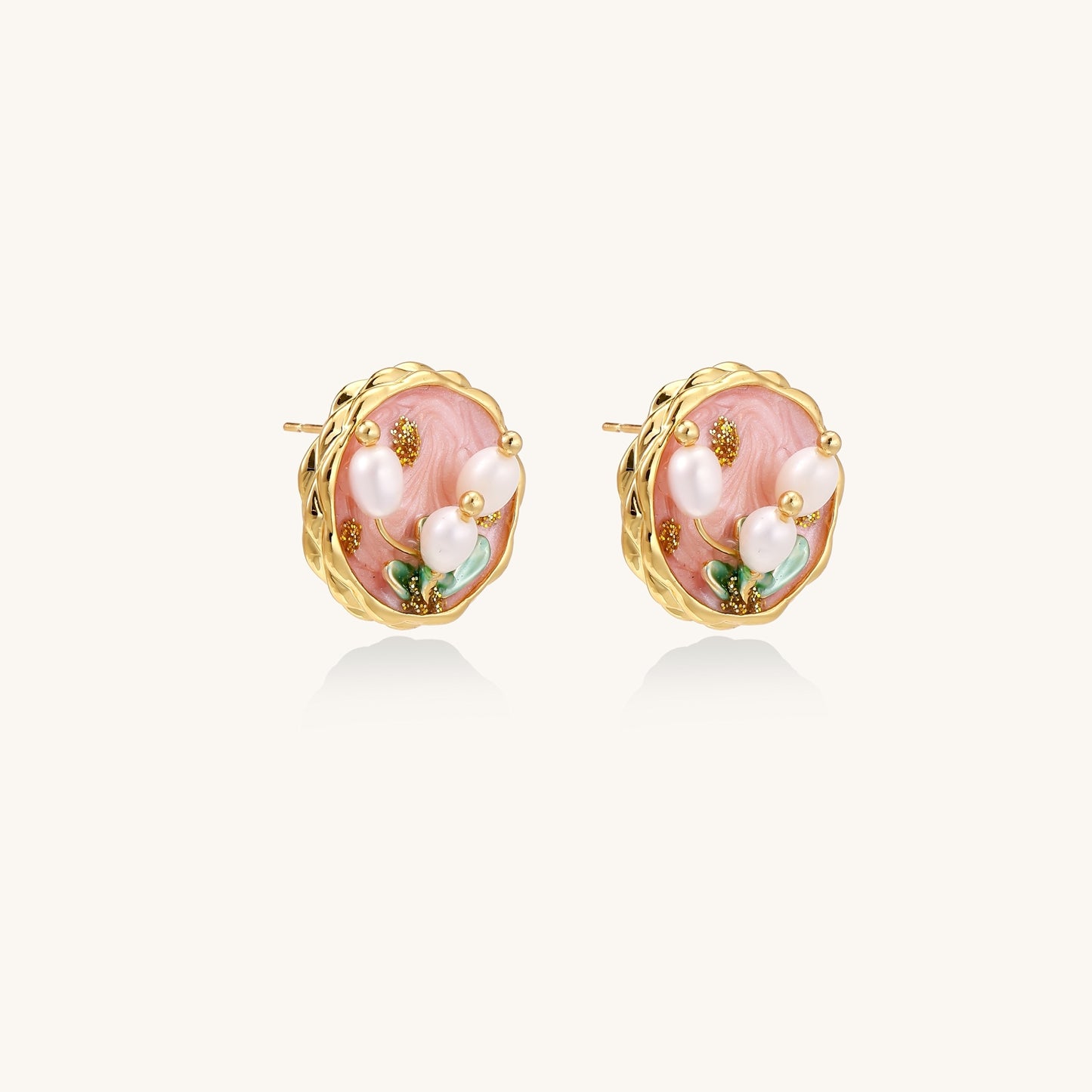 Round stud earrings with pink enamel background, white pearl tulips, green leaves, and twisted gold border on white background.