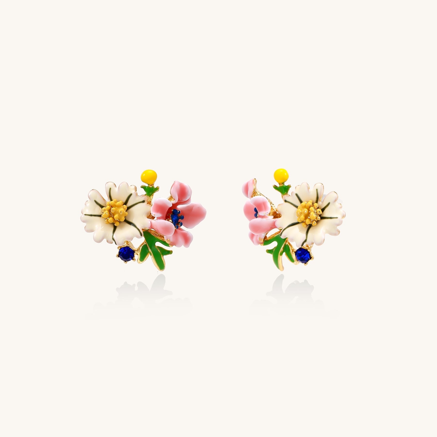 Detailed view of gold-plated brass stud earrings featuring multicolor enamel flowers with white, pink, and blue petals