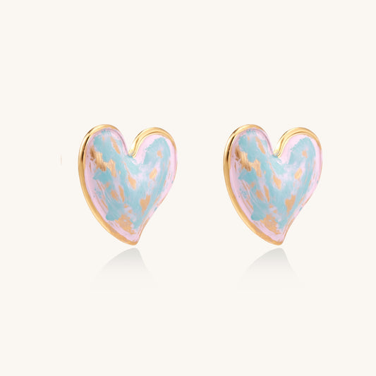 Heart-shaped stud earrings with iridescent blue-pink enamel finish and gold-plated brass frames against cream background