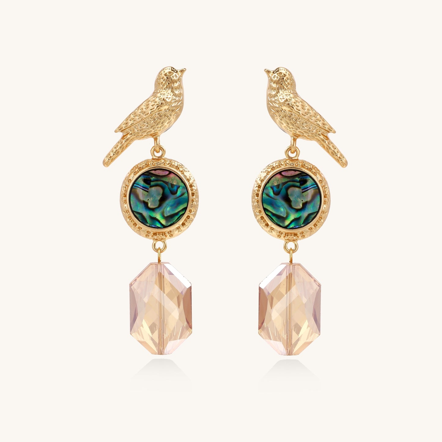 Gold-plated bird dangle earrings with iridescent abalone shell discs and champagne crystal drops on white background.