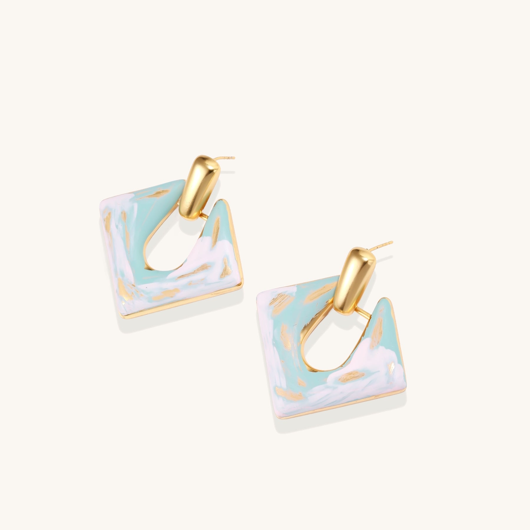 Diamond-shaped gold-plated earrings with pastel marble enamel in turquoise and lavender swirls on beige background