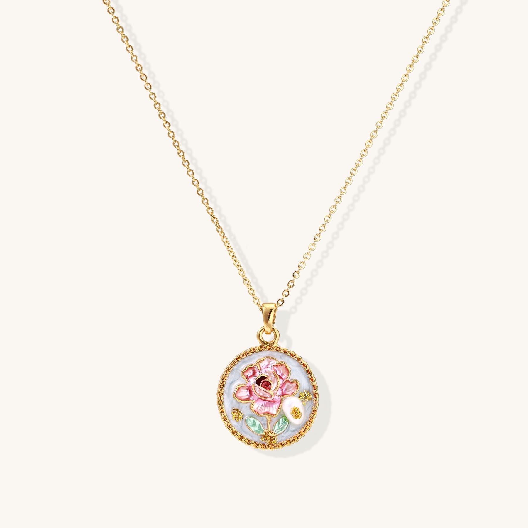 Gold-plated circular pendant featuring pink enamel rose with pearl accents and green leaf details on adjustable chain.