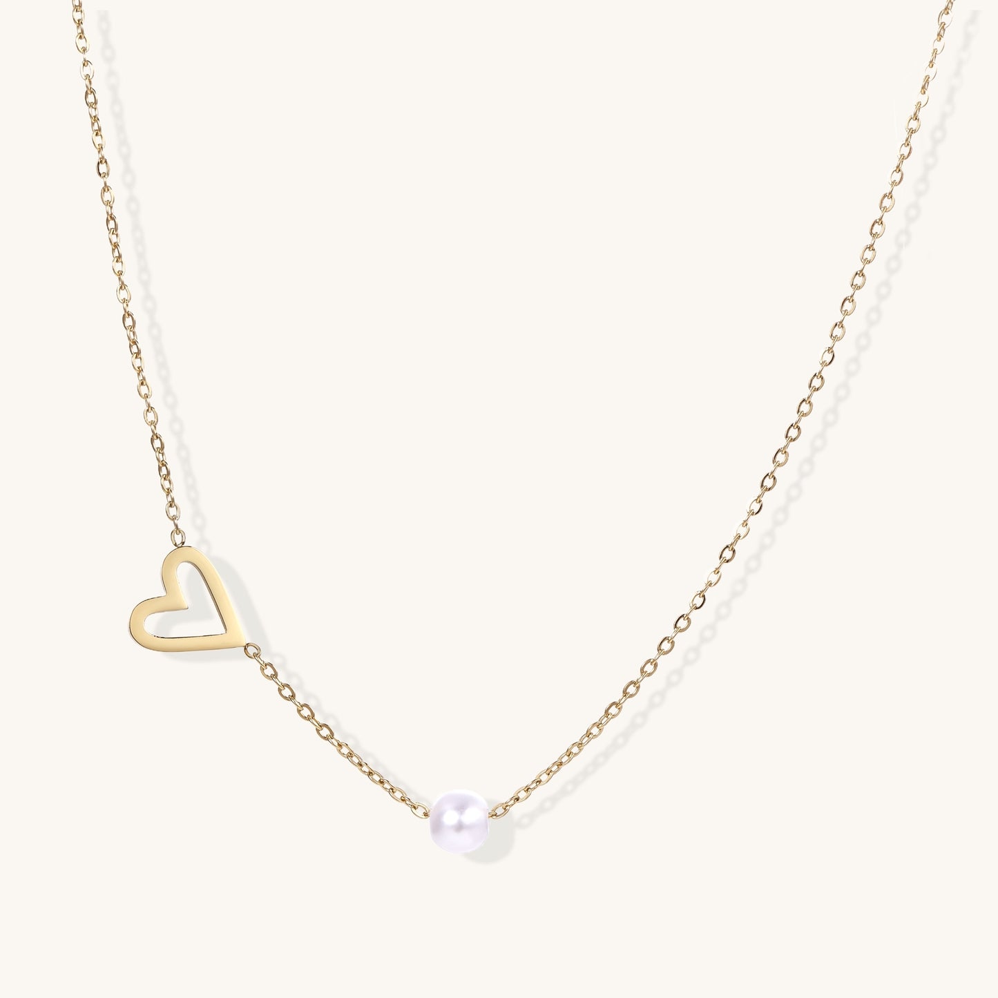 Dainty 14K gold-plated necklace with open heart pendant and white pearl bead on neutral background