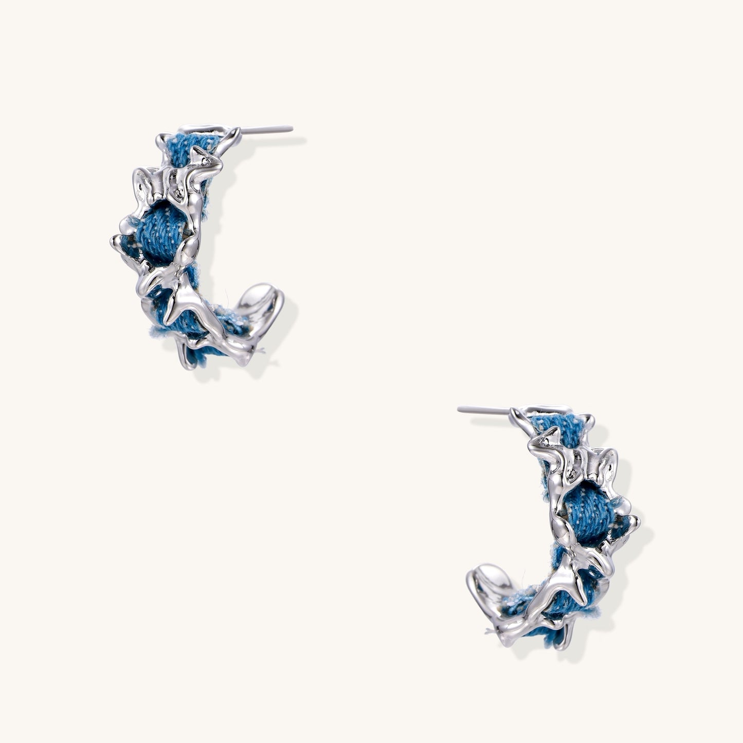 Crescent-shaped gold-plated hoop earrings with blue crystals set in organic vine-like metalwork on white background.