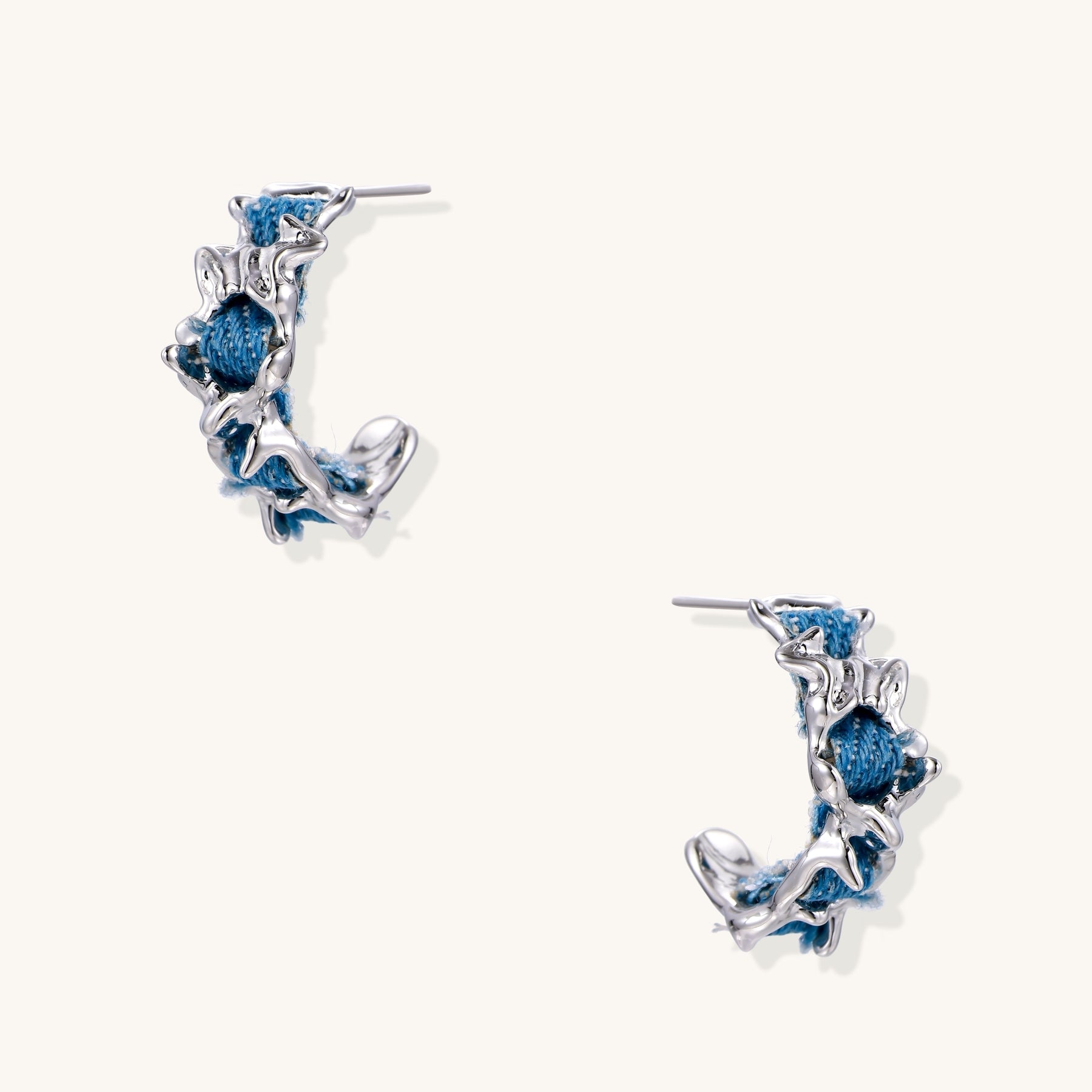 Crescent-shaped gold-plated hoop earrings with blue crystals set in organic vine-like metalwork on white background.