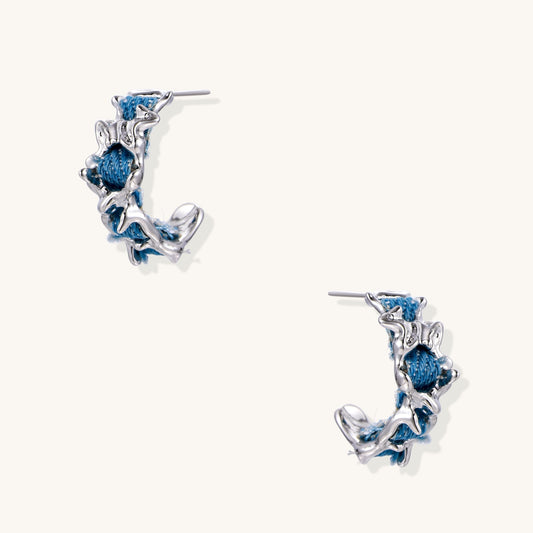Crescent-shaped gold-plated hoop earrings with blue crystals set in organic vine-like metalwork on white background.