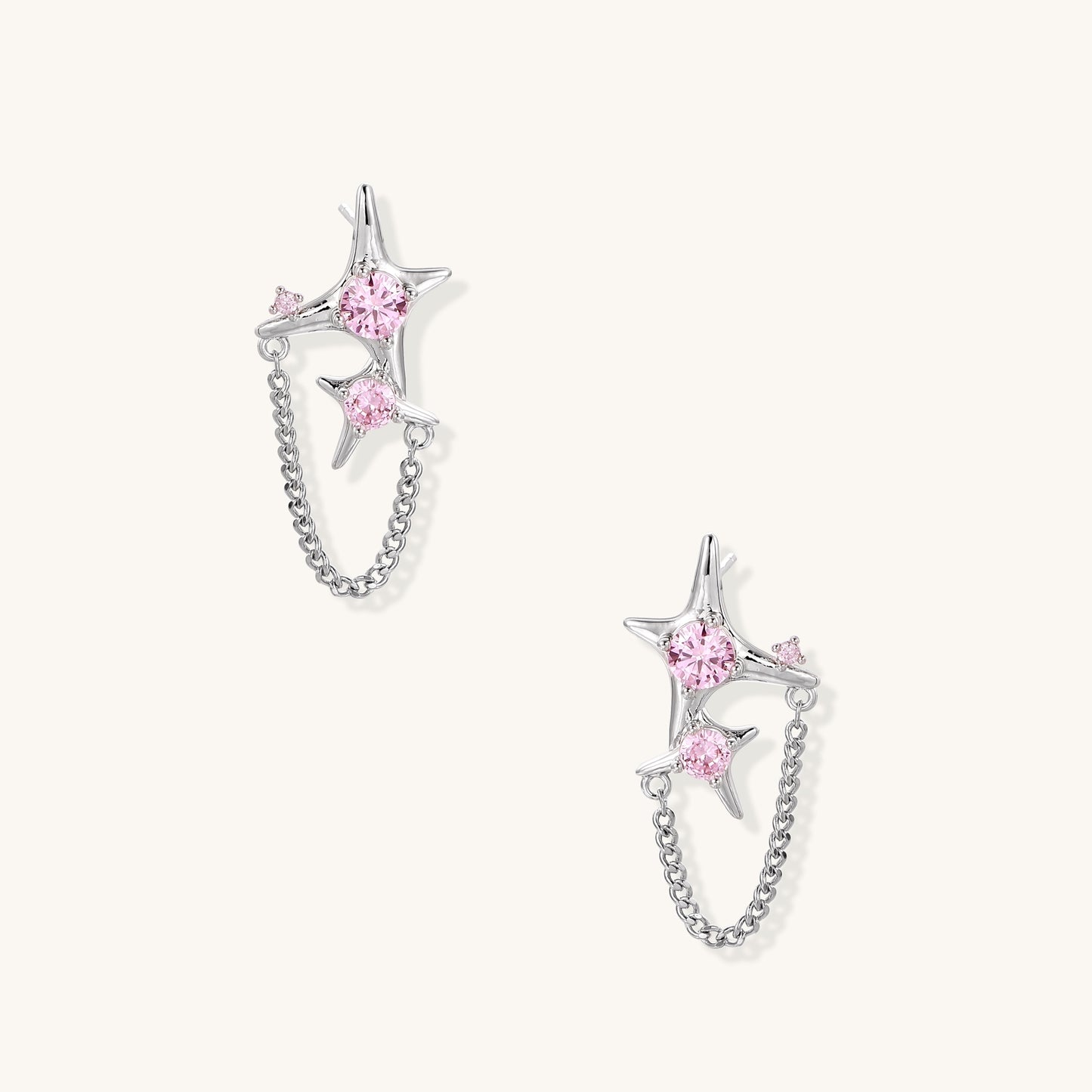 Gold-plated star earrings with pink zirconia stones connected by delicate chains on light background