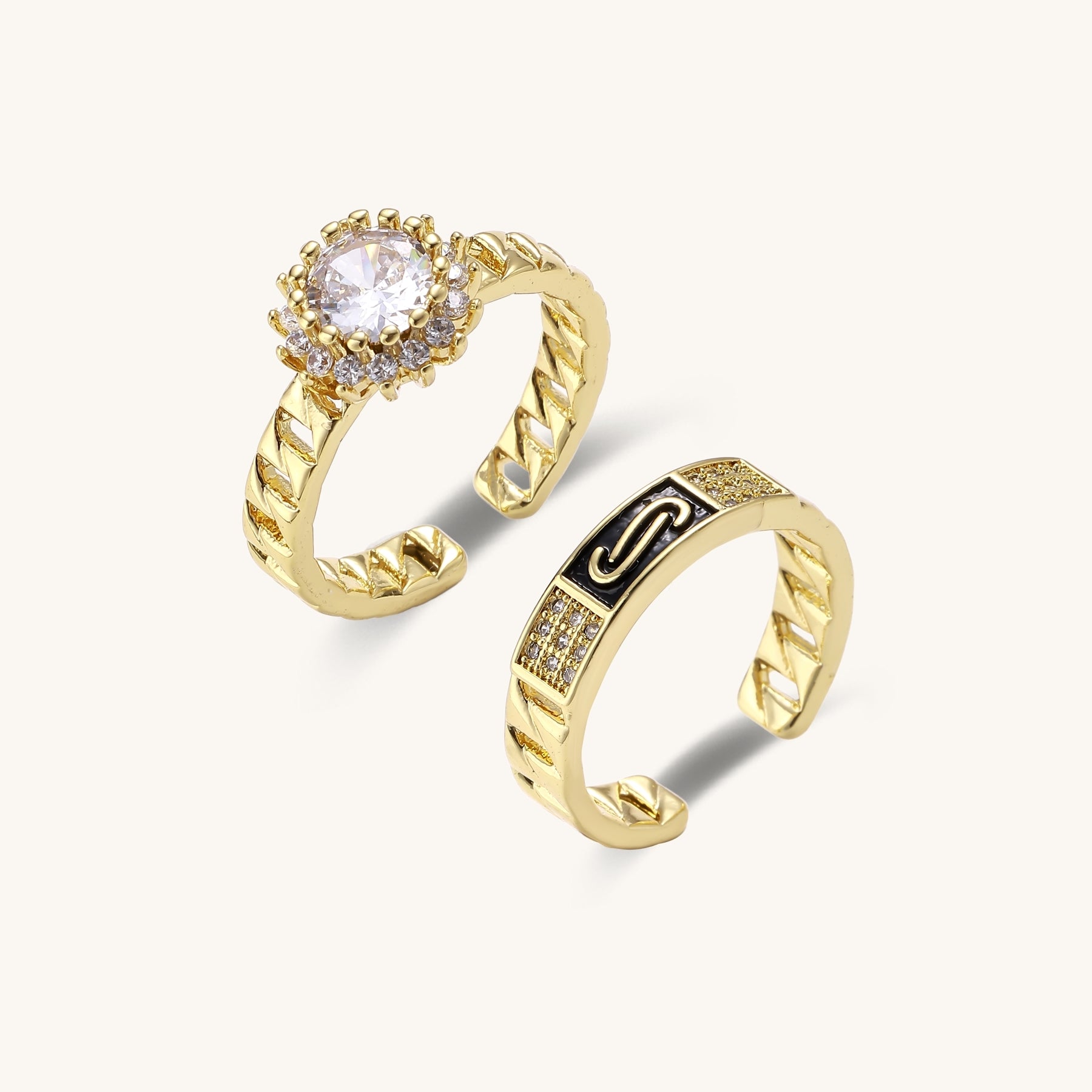 Two gold-plated brass rings with chain-link bands, one featuring a round cubic zirconia halo, one with black enamel accent.