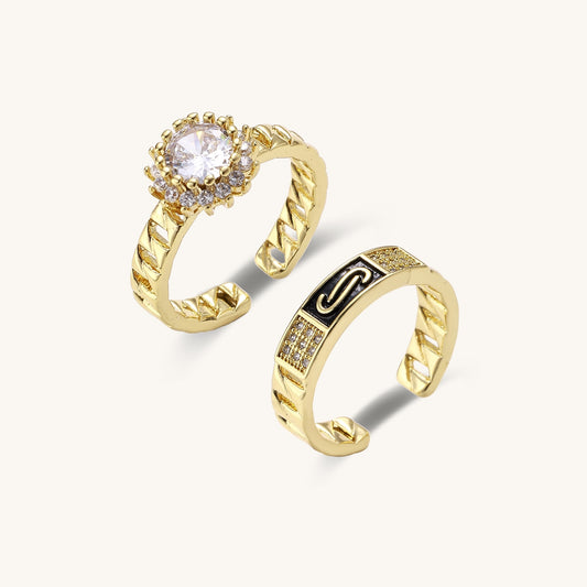 Two gold-plated brass rings with chain-link bands, one featuring a round cubic zirconia halo, one with black enamel accent.