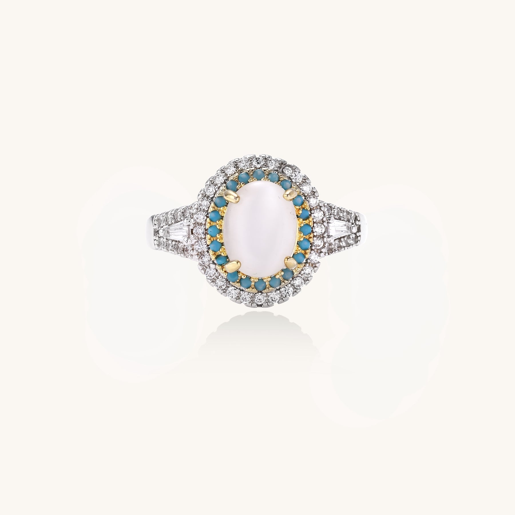 Gold-plated ring with oval cat's eye stone center, blue accent stones, and crystal halo on white background.