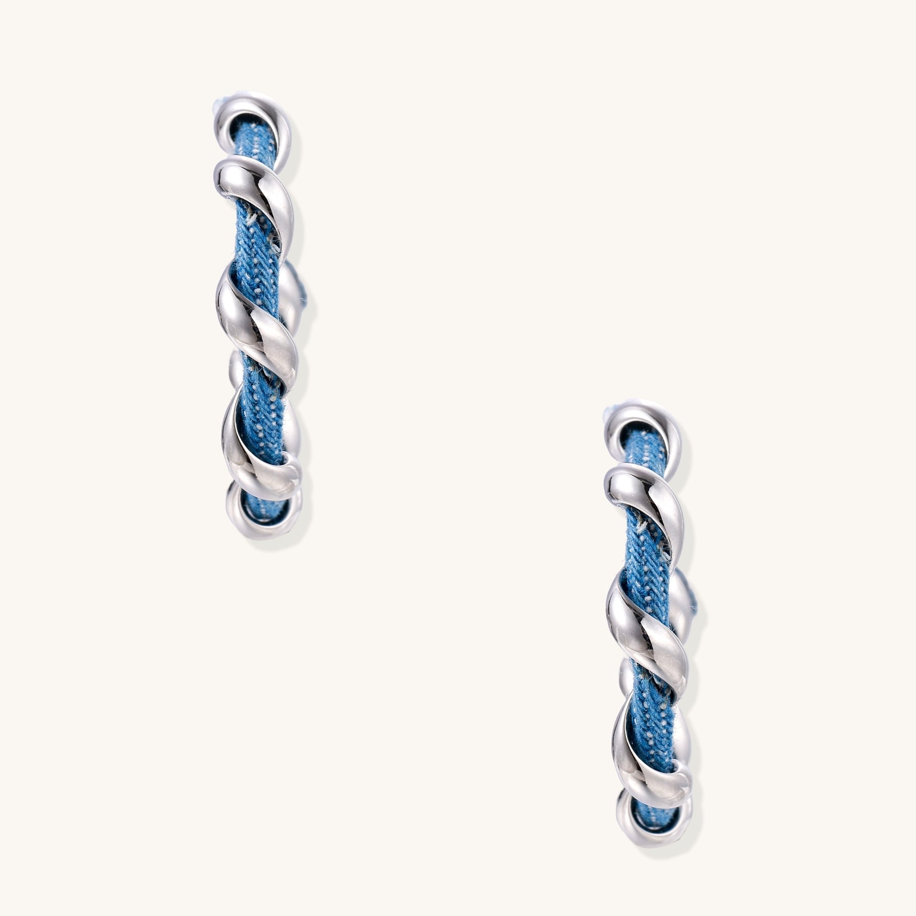 Twisted hoop earrings featuring blue denim fabric braided with gold-plated metal in a spiral design on white background.