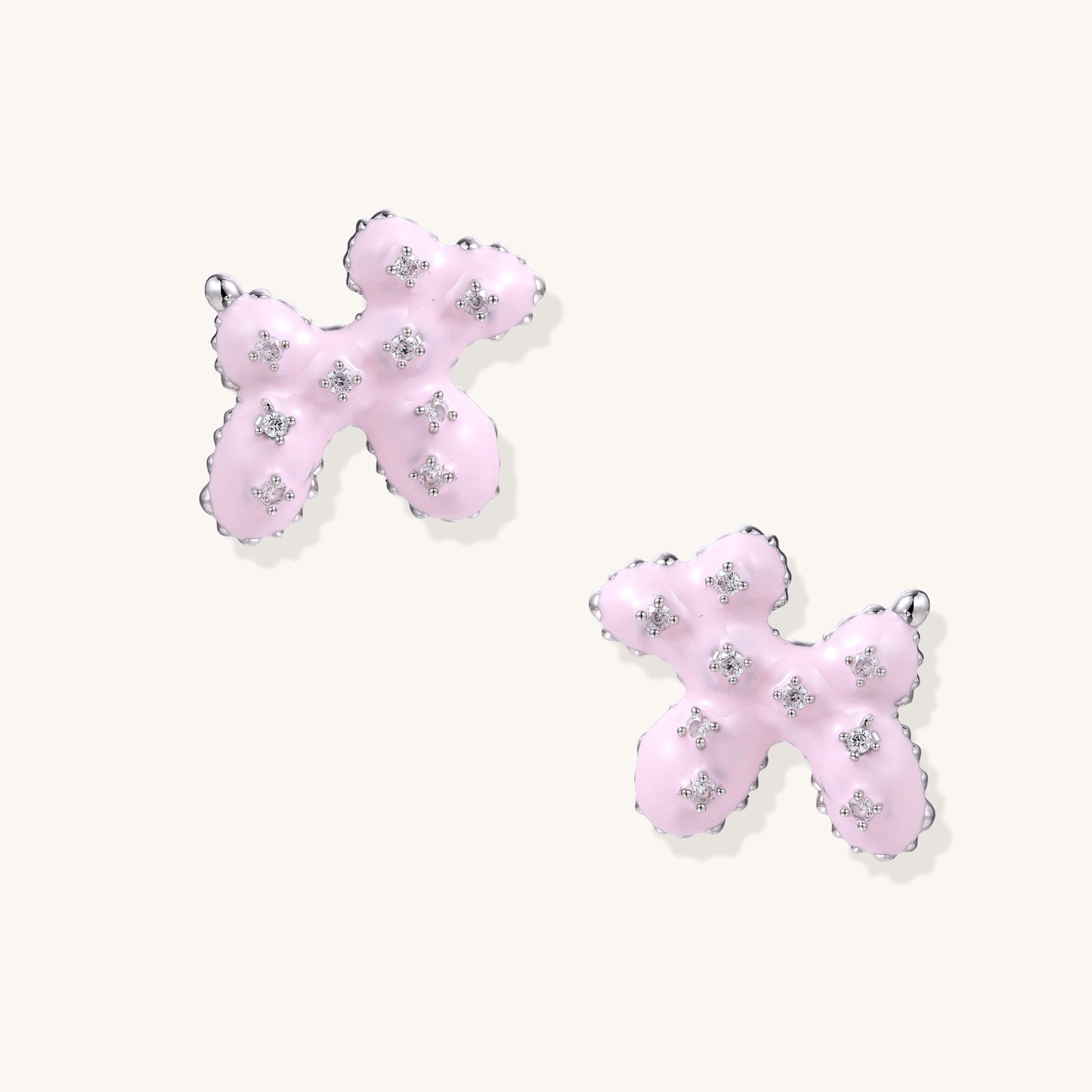 Pair of pink enamel flower-shaped stud earrings with zirconia crystal accents on cream background