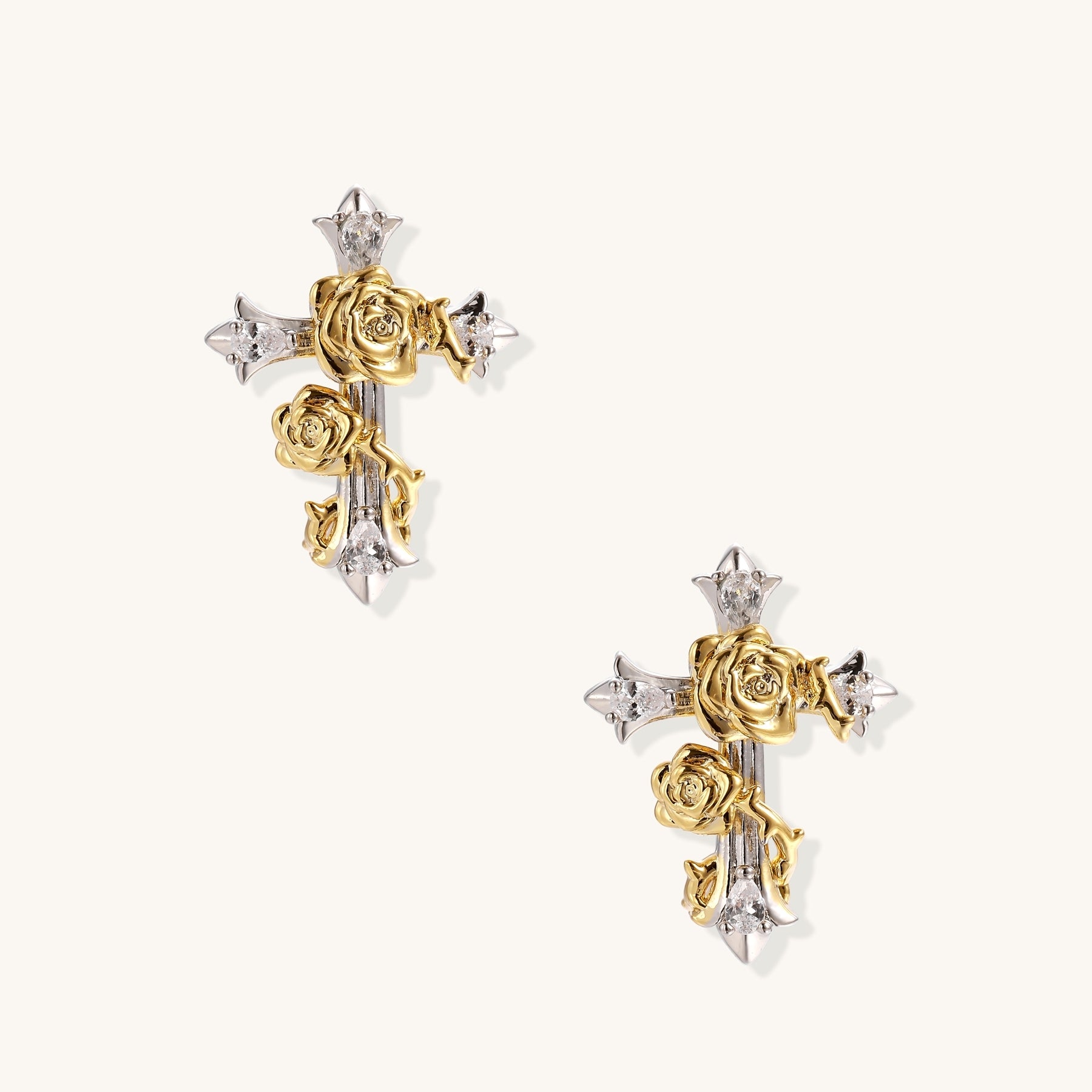 Two-tone cross earrings with gold roses and silver base featuring crystal accents on beige background.