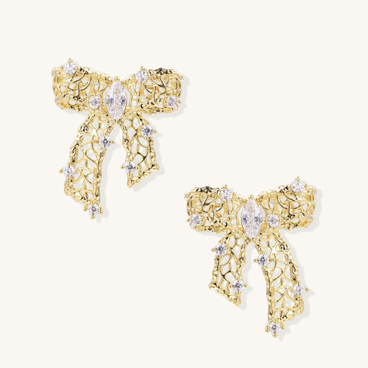 Gold and silver bow-shaped earrings with intricate lattice pattern and clear zirconia stones on neutral background.