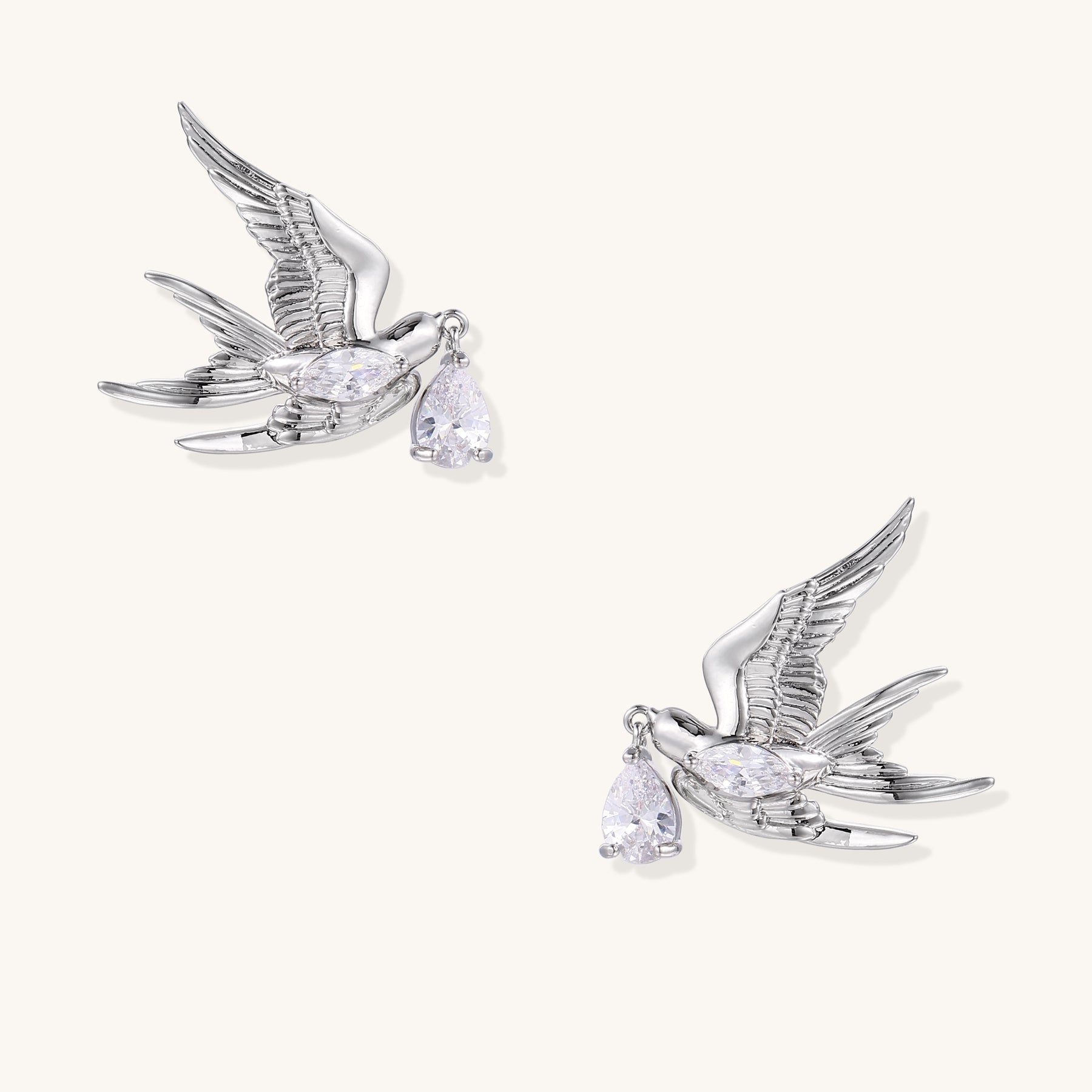 Gold-plated brass swallow earrings with detailed wing engravings carrying clear zirconia crystal drops in their beaks