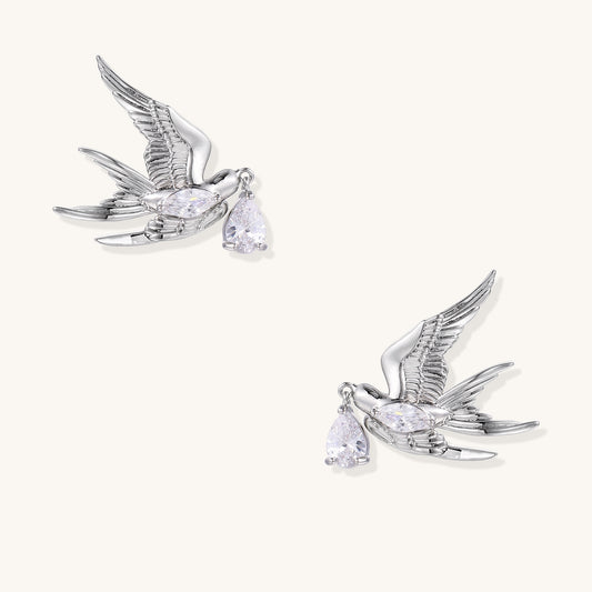 Gold-plated brass swallow earrings with detailed wing engravings carrying clear zirconia crystal drops in their beaks