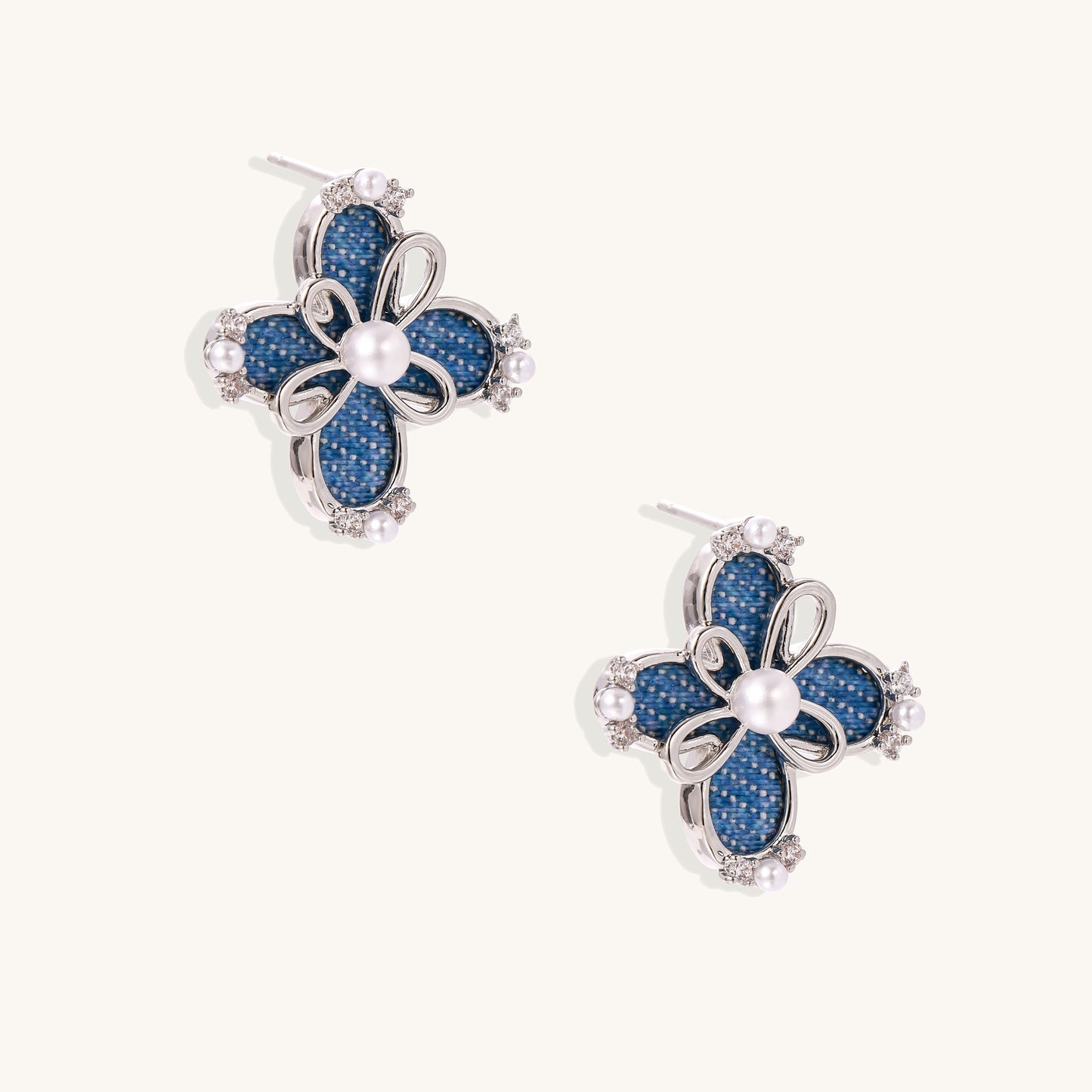 Blue denim flower stud earrings with silver framework, white pearl centers, and crystal accents on cream background.